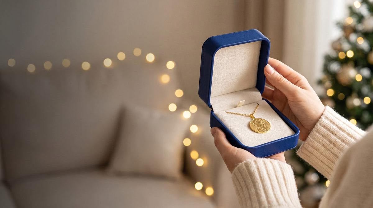 A gold saint medal in an open navy gift box, held in two hands